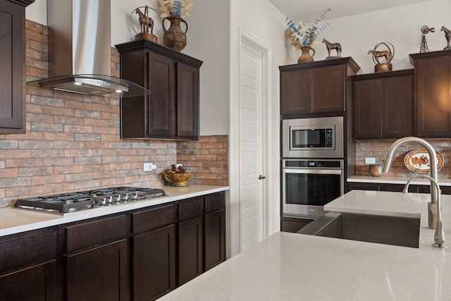 kitchen featuring tasteful backsplash, a sink, dark brown cabinetry, wall chimney exhaust hood, and appliances with stainless steel finishes