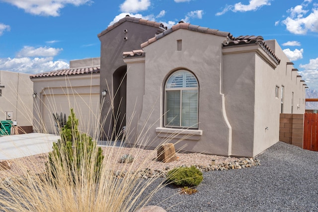 view of front facade featuring a tiled roof, driveway, fence, an attached garage, and stucco siding