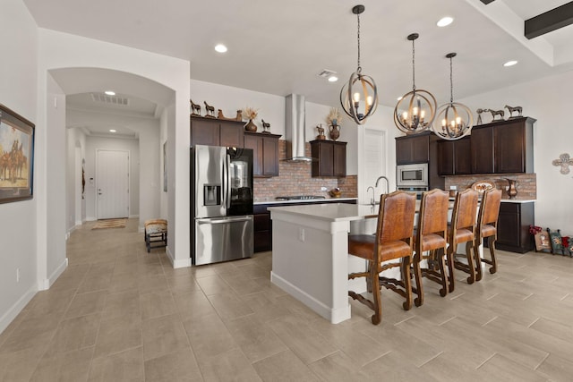 kitchen featuring dark brown cabinetry, a kitchen breakfast bar, stainless steel appliances, light countertops, and wall chimney range hood