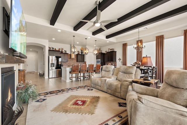 living room with recessed lighting, arched walkways, beamed ceiling, a lit fireplace, and ceiling fan with notable chandelier