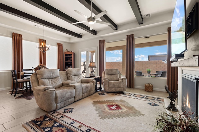 living room featuring ceiling fan with notable chandelier, visible vents, baseboards, a lit fireplace, and beamed ceiling