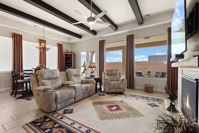 living room featuring visible vents, beam ceiling, baseboards, a lit fireplace, and ceiling fan with notable chandelier