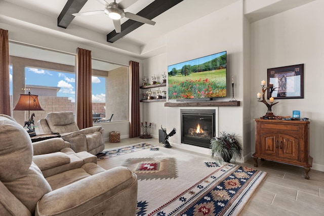 living area with ceiling fan, baseboards, a glass covered fireplace, and beam ceiling