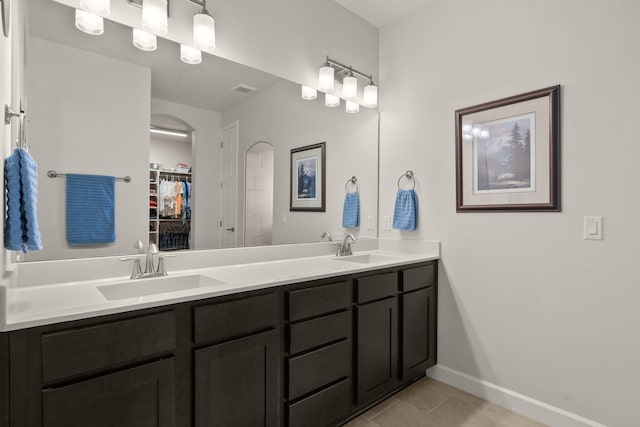 bathroom with a sink, a spacious closet, baseboards, and double vanity