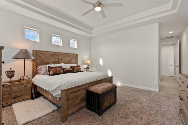 carpeted bedroom featuring a ceiling fan, a tray ceiling, visible vents, and baseboards