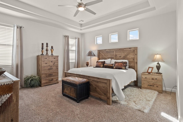 carpeted bedroom with a ceiling fan, a raised ceiling, visible vents, and baseboards