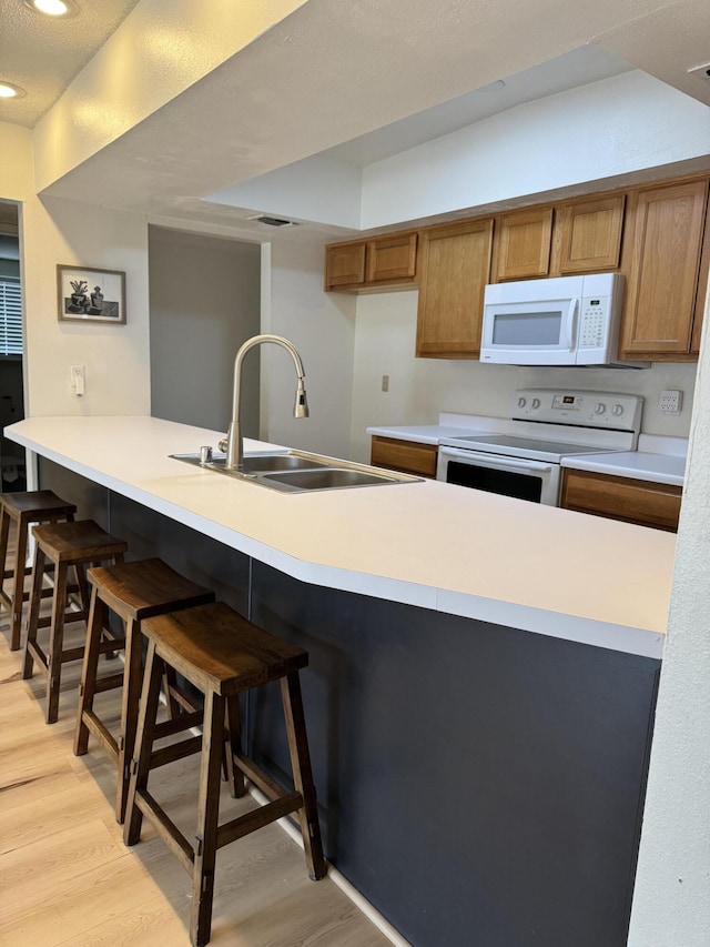 kitchen featuring white appliances, a kitchen breakfast bar, sink, light hardwood / wood-style flooring, and kitchen peninsula