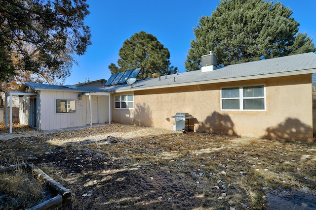 rear view of property with roof mounted solar panels and a chimney