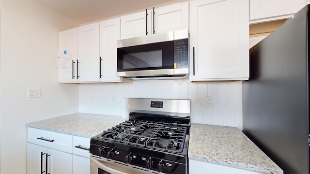 kitchen featuring decorative backsplash, white cabinetry, light stone countertops, and appliances with stainless steel finishes