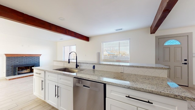 kitchen featuring white cabinets, light stone counters, stainless steel dishwasher, sink, and a fireplace