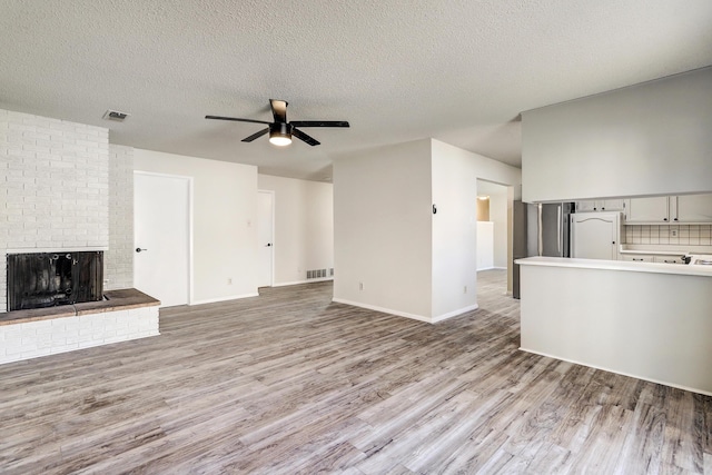 unfurnished living room with a fireplace, a textured ceiling, light hardwood / wood-style floors, and ceiling fan