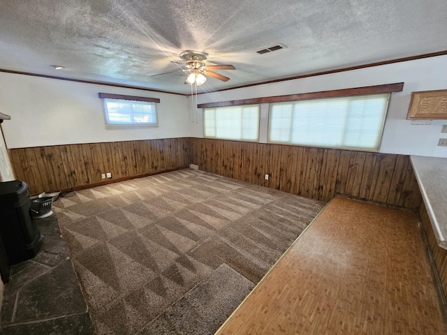 interior space with crown molding, wood walls, a textured ceiling, and a wood stove