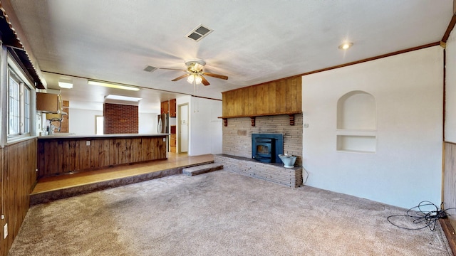 unfurnished living room with built in features, carpet floors, a wood stove, ornamental molding, and ceiling fan