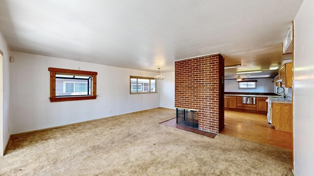 unfurnished living room with light carpet, a brick fireplace, sink, and a chandelier