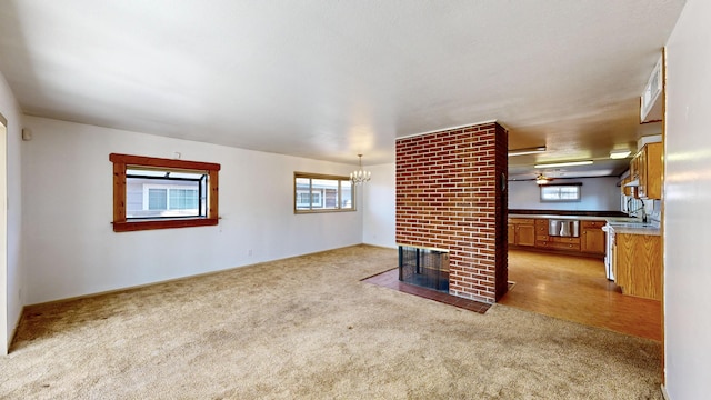 unfurnished living room with light carpet, a brick fireplace, sink, and a chandelier