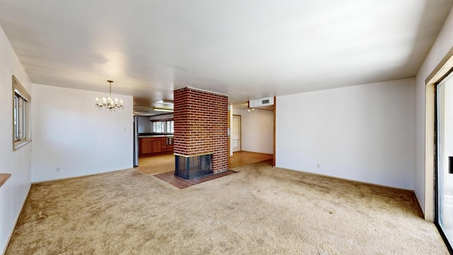 unfurnished living room with a brick fireplace, a notable chandelier, and carpet flooring