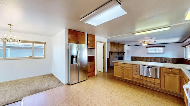 kitchen with a brick fireplace, hanging light fixtures, a textured ceiling, stainless steel fridge, and ceiling fan with notable chandelier