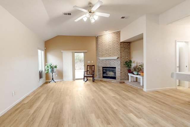 unfurnished living room with ceiling fan, vaulted ceiling, a brick fireplace, and light wood-type flooring