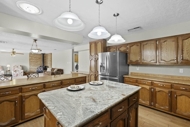 kitchen featuring a wood stove, hanging light fixtures, a center island, stainless steel refrigerator with ice dispenser, and light wood-type flooring