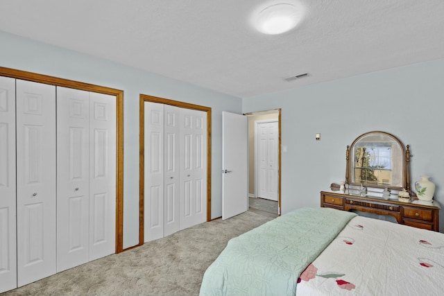 bedroom featuring a textured ceiling, light colored carpet, and multiple closets