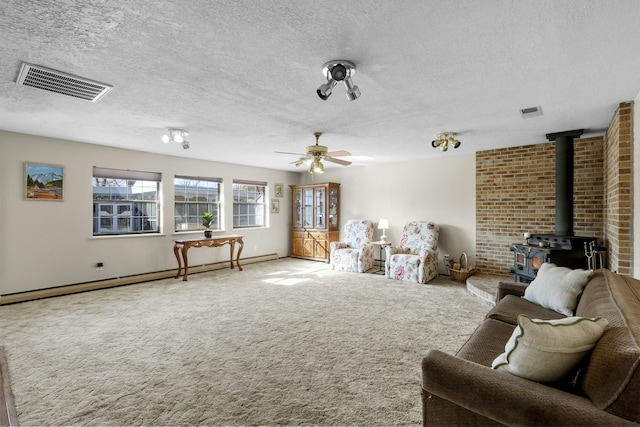 living room with a textured ceiling, a wood stove, a baseboard radiator, ceiling fan, and carpet