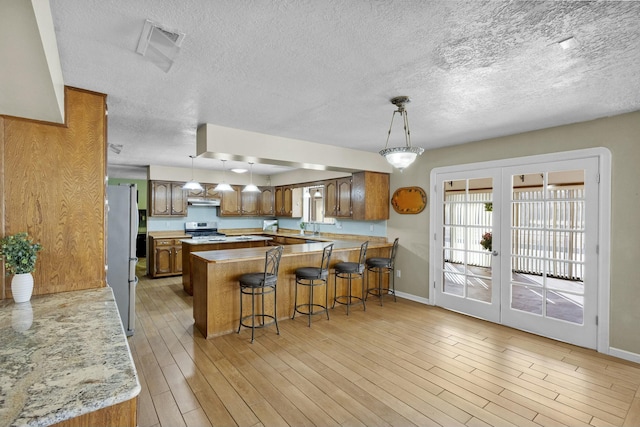 kitchen with appliances with stainless steel finishes, sink, a kitchen breakfast bar, light hardwood / wood-style floors, and french doors