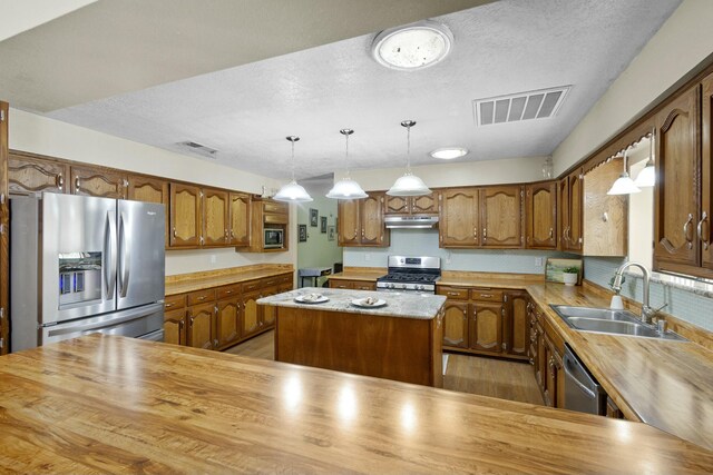 kitchen with sink, a center island, hanging light fixtures, a textured ceiling, and stainless steel appliances