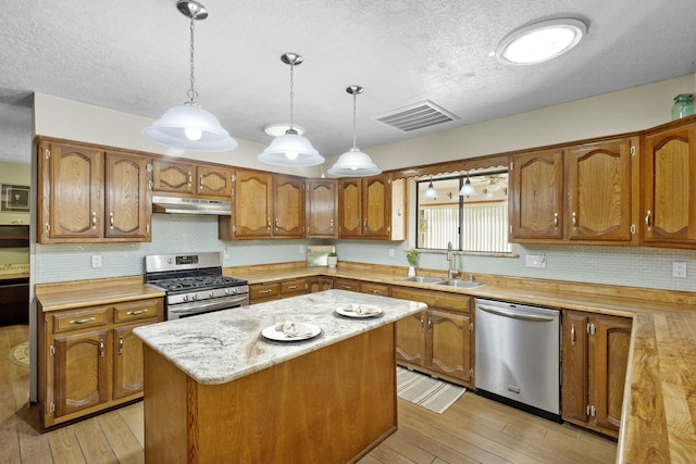 kitchen with appliances with stainless steel finishes, pendant lighting, sink, a center island, and light wood-type flooring