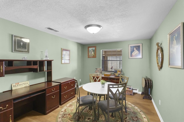 dining room featuring a baseboard heating unit, a textured ceiling, and light wood-type flooring