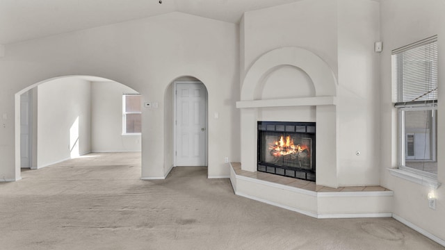 unfurnished living room with light colored carpet, a tiled fireplace, and vaulted ceiling