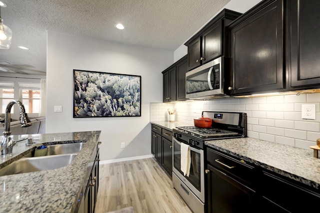 kitchen with light wood-type flooring, tasteful backsplash, a textured ceiling, stainless steel appliances, and sink