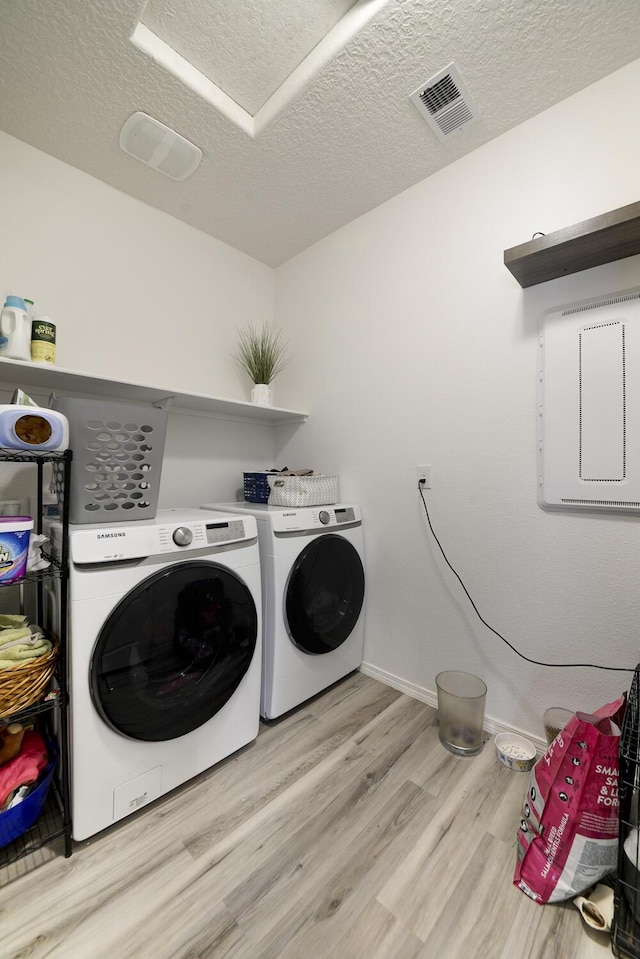 clothes washing area featuring washing machine and dryer, light hardwood / wood-style floors, and a textured ceiling