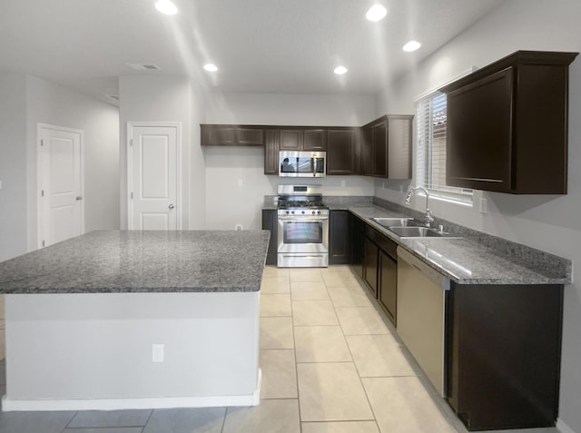 kitchen featuring appliances with stainless steel finishes, dark stone counters, sink, light tile patterned floors, and a center island