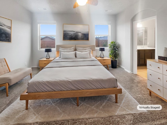 carpeted bedroom with ensuite bath, ceiling fan, and multiple windows