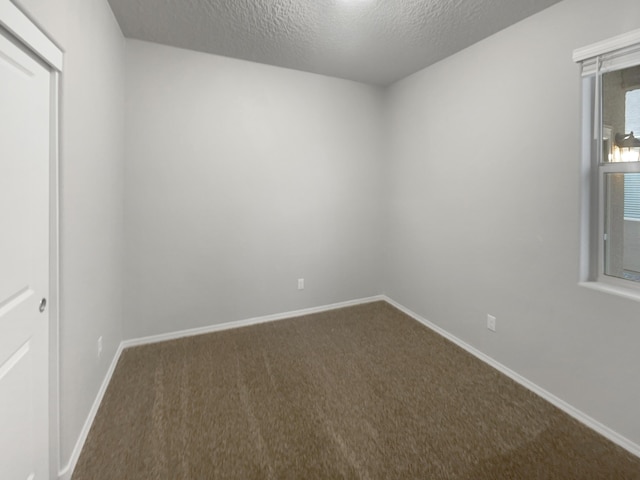 spare room with a textured ceiling and dark colored carpet