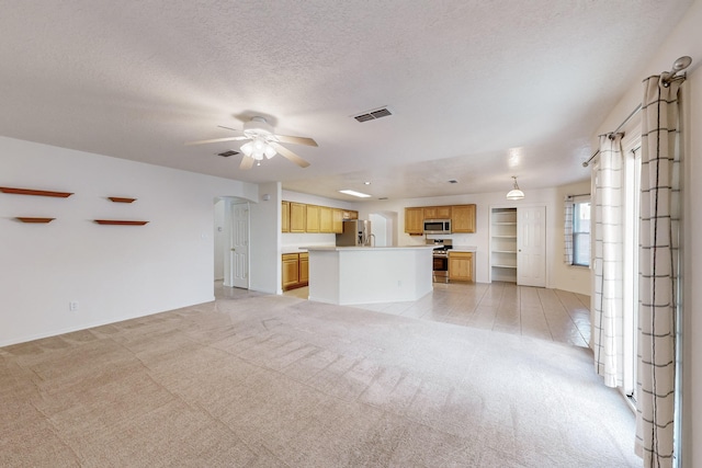 unfurnished living room with ceiling fan, a textured ceiling, and light carpet