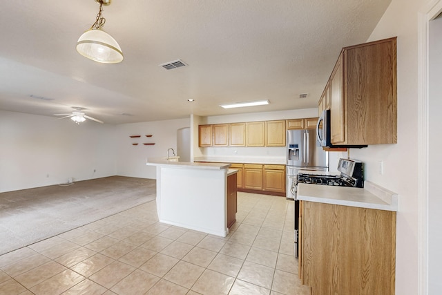 kitchen featuring a textured ceiling, light colored carpet, stainless steel appliances, pendant lighting, and a center island with sink