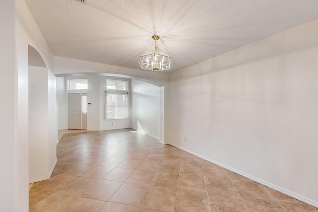 empty room with light tile patterned floors, a textured ceiling, and an inviting chandelier