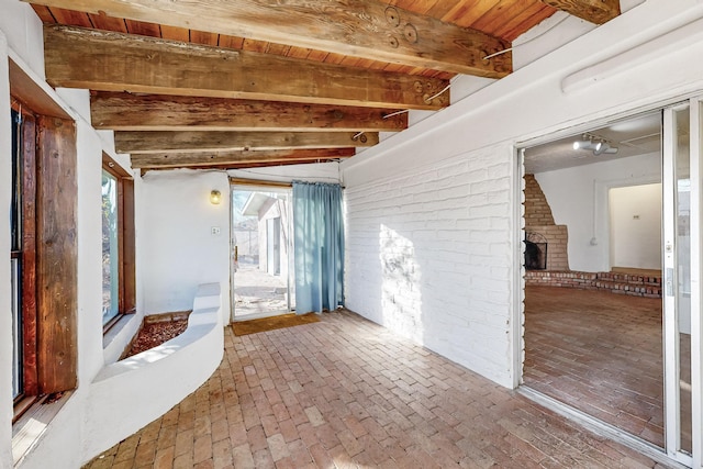 unfurnished room with beamed ceiling, brick wall, wood ceiling, and a fireplace