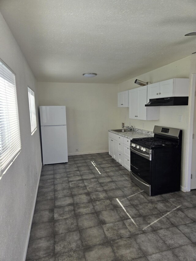 kitchen featuring sink, stainless steel gas range oven, a textured ceiling, white cabinets, and white fridge