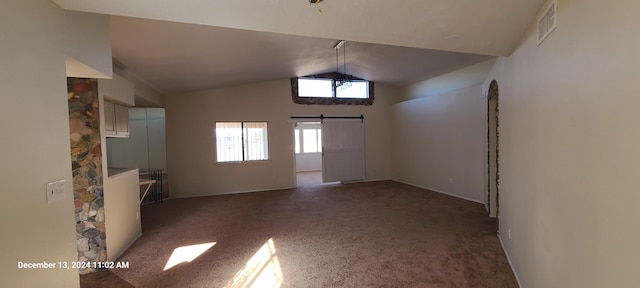 carpeted empty room with a barn door and lofted ceiling