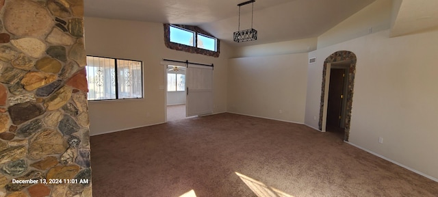 carpeted empty room featuring a barn door and vaulted ceiling