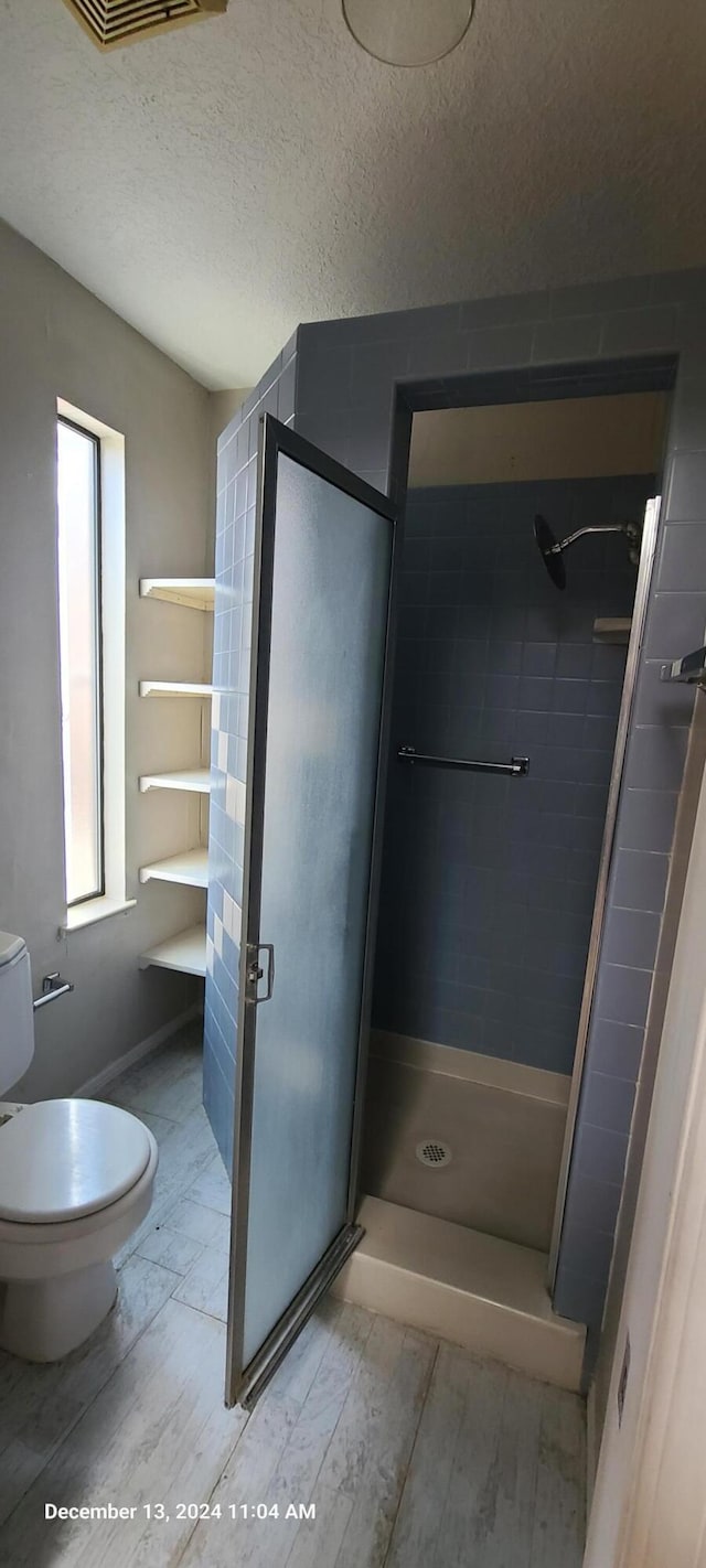 bathroom featuring hardwood / wood-style flooring, toilet, a tile shower, and a textured ceiling