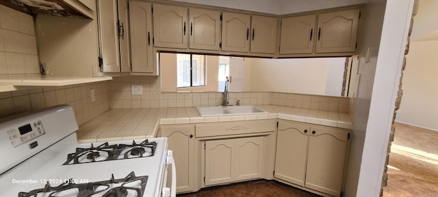 kitchen with tasteful backsplash, tile counters, gas range gas stove, and sink