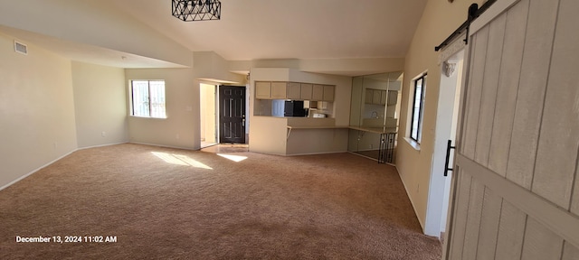 unfurnished living room featuring a barn door, light colored carpet, and vaulted ceiling