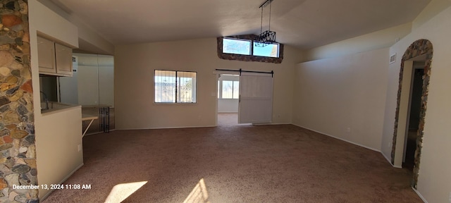 unfurnished living room with dark colored carpet, a barn door, and lofted ceiling