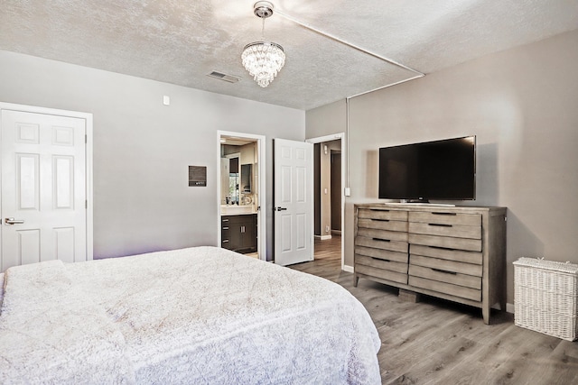 bedroom featuring a chandelier, a textured ceiling, hardwood / wood-style flooring, and ensuite bathroom