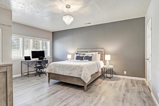 bedroom with a chandelier, a textured ceiling, and light wood-type flooring