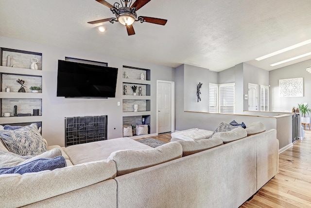 living room with ceiling fan, light wood-type flooring, a textured ceiling, and vaulted ceiling