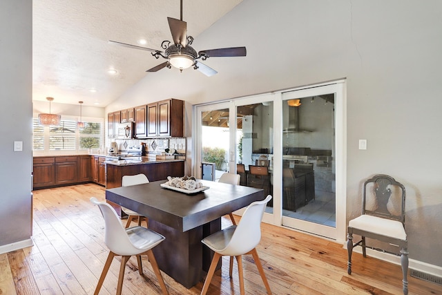 dining space featuring a textured ceiling, light wood-type flooring, vaulted ceiling, and ceiling fan